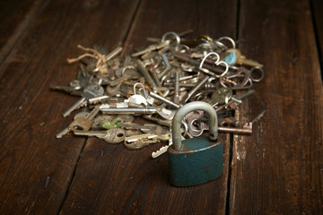 Pile of keys and lock on a grunge wooden background.