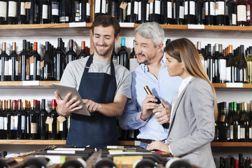 Salesman Showing Wine Information To Couple On Digital Tablet