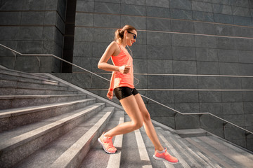 Young sports woman running down the stairs in the modern city. Healthy lifestyle and morning jogging in the city