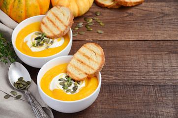 Pumpkin cream soup with cream and pumpkin seeds on wooden background, selective focus, copy space