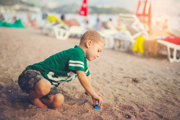 Kid playing with toy cars sitting outdoors at pebble beach 