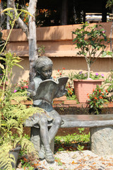 Bronze statue of a girl reading a book in the garden.