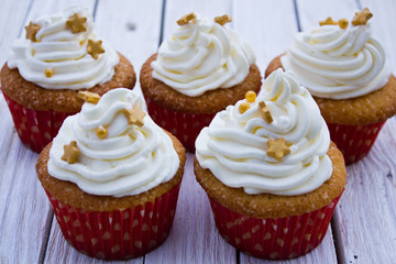 Cupcakes with mascarpone cream and gold decoration on a white wooden table.