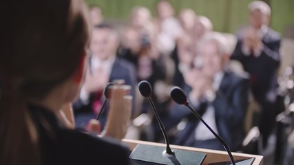 Over the shoulder shot with selective focus of female politician making statement before supporting and applauding public