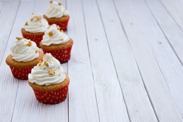 Cupcakes with mascarpone cream and gold decoration on a white wooden table.