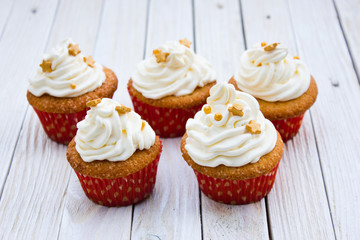 Cupcakes with mascarpone cream and gold decoration on a white wooden table.