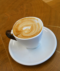 Delicious foamy cappuccino on a white cup on a plate