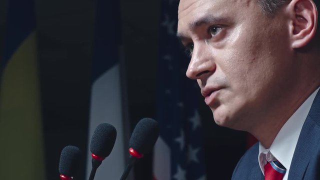 Closeup profile shot of assertive male politician speaking into microphones on political convention 