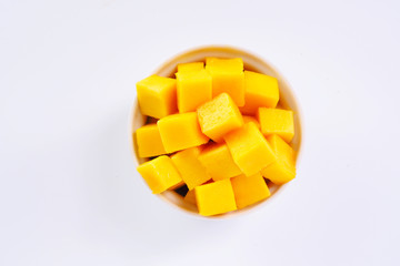 Top view of diced ripe mango cube in a white bowl on a white background. 