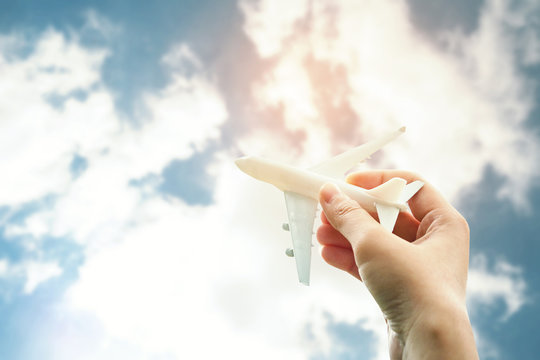 man's hand holding toy airplane against blue sky with clouds vintage tone and soft focus