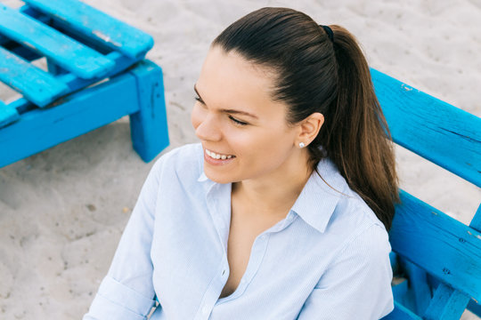 Cute young brunette woman sitting on a bench on the beach and sm