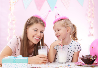 Young pretty mom with cute daughter drinking milk cocktail celebrating birthday. Concept of annual tradition and lifestyle.