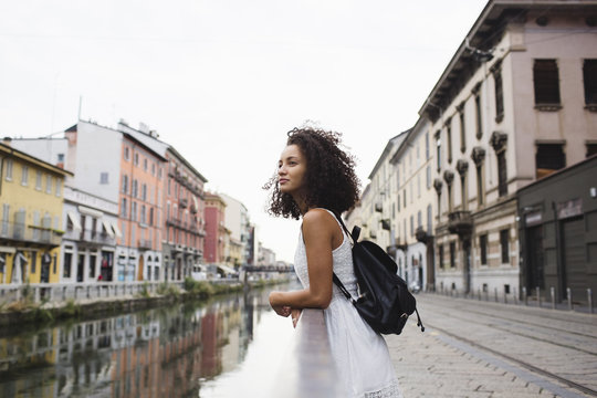 Italy, Milan, young woman with backpack leaning on railing looking at distance