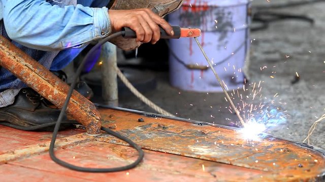 A man welding steel on the part of fishing boat at the harbor