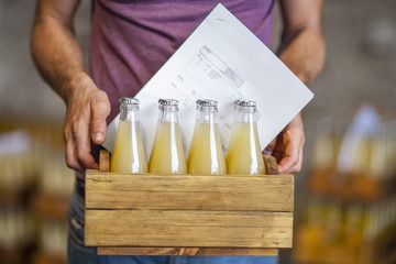 Man carrying wooden box with bottles of juice in warehouse