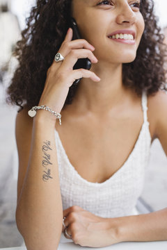 Smiling young woman with tattoo on forearm on the phone