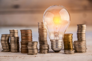 glowing light bulb among many coins