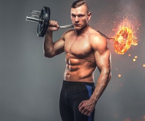 Athletic male holds the burning barbell.