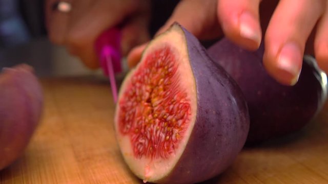 Girl cutting ripe fig on wooden board. 4K close up pan video