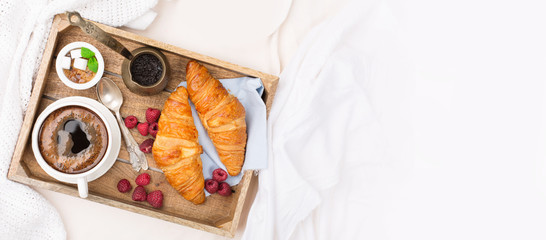 Morning breakfast in bed with cup of coffee, croissants, fresh berries and honey on wooden tray, selective focus