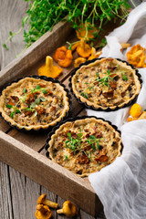 Homemade tarts of puff pastry with seasonal chanterelle mushrooms, cheese, thyme and onion on rustic wooden table, selective focus