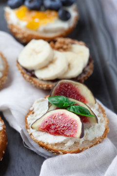Bagels with different toppings - with cream cheese, figs, bananas, chocolate and blueberries for breakfast on a tray, selective focus