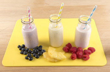 Image of three smoothies in glass bottles on a yellow chopping board, with mixed fruit in front of the drinks. 