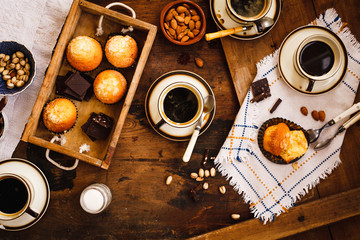 Breakfast Table with coffee cup, nuts, chocolate and breakfast muffins spread over old wooden tabletop. 