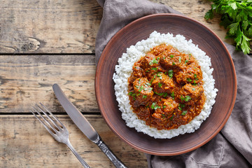 Madras butter Beef spicy Indian garam masala slow cook lamb food with rice and tomatoes in clay plate on vintage wooden table background. Delicious India culture restaurant dish.