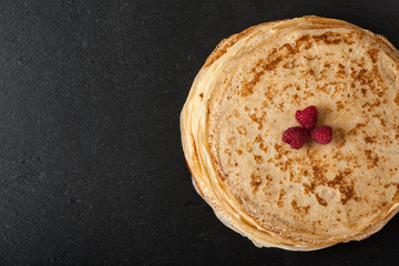 Stack of pancakes with raspberries on black