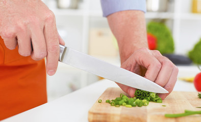 Closeup man's hands chopping green onion on a wooden chopping board with knife.