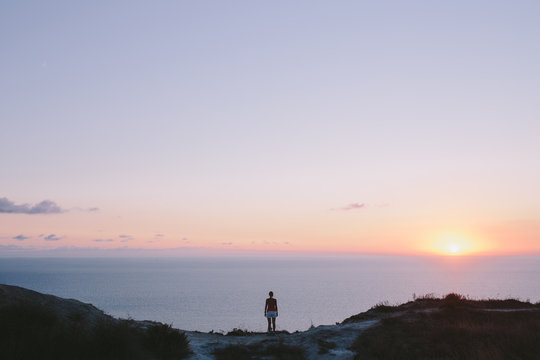 Young woman hiker standing on hill and looking to forward at sea. back view