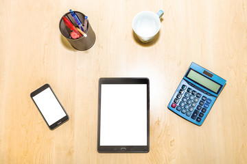 Flat lay of a business and finance desktop with tools: pad, calculator, penholder,coffee cup, and tablet on wooden table. Blank white screen for copy space