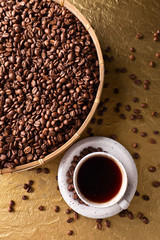 Cup of black coffee and  beans on a golden background