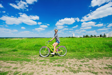 Obraz premium Beautiful girl riding bicycle outdoors across the green sunny field