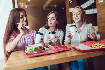 Three cheerful young girls eating fast food in a restaurant