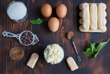 Ingredients of traditional italian dessert tiramisu - ladyfingers cake, eggs, sugar, mascarpone creme, cocoa, chocolate and peppermint on wooden background, top 
