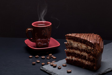 Piece of chocolate cake and cup of coffee on slate plate on blac