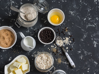 Baking background. Flour, sugar, butter, rolled oats, eggs, chocolate chips on a dark background. Baking ingredients