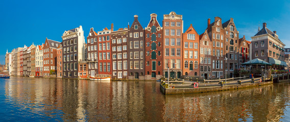 Fototapeta premium Panorama pięknych, typowych holenderskich domów tanecznych nad kanałem Amsterdam Damrak w słoneczny dzień, Holandia, Holandia.
