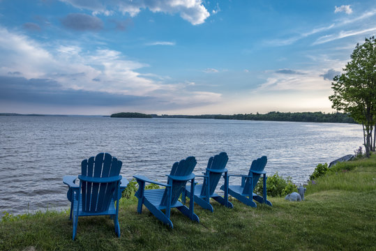 row of blue wooden cottage chairs facing lake