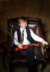 Freckled red-hair boy with violin sitting in the arm-chair
