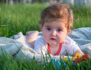 Little girl (six months old) with beautiful blue eyes is lying on the green grass in the park.