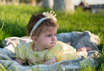 A little girl (six months old) with a crown on her head is lying on the lawn.  She's unhappy and going to cry.
