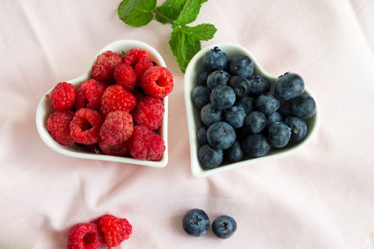 Picture of two heart shaped plate filled with blueberries and raspberries and mint leaves. 
