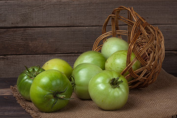 unripe green tomatoes in a wicker basket on  wooden background and sackcloth