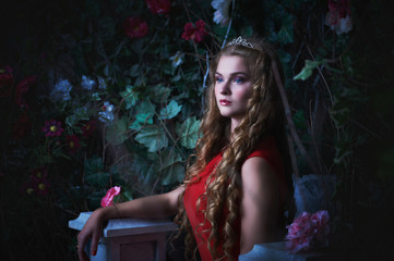 Fototapeta na wymiar Fairy tale. Beautiful princess in red dress sitting in a mystical garden