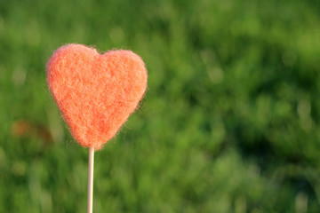 Pink heart made of cloth (fabric) on a stick on a background of green grass