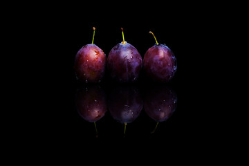 Three fresh blue plums on a black reflective background with water drops