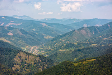 Naklejka premium wieś na łące na zboczu wzgórza z lasem w górach o wschodzie słońca